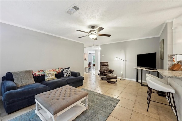 living area featuring ceiling fan, visible vents, crown molding, light tile patterned floors, and baseboards