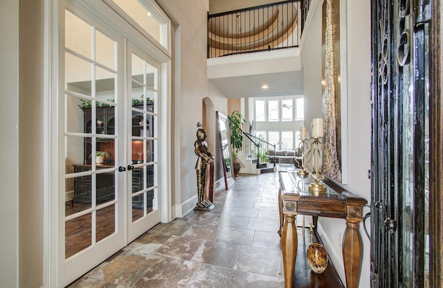 entryway with stone finish flooring, baseboards, french doors, a towering ceiling, and arched walkways
