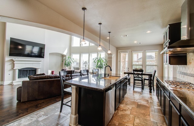 kitchen featuring a sink, decorative backsplash, stainless steel appliances, a kitchen bar, and wall chimney exhaust hood
