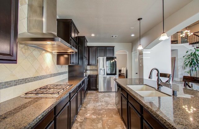 kitchen featuring visible vents, appliances with stainless steel finishes, arched walkways, wall chimney exhaust hood, and a sink