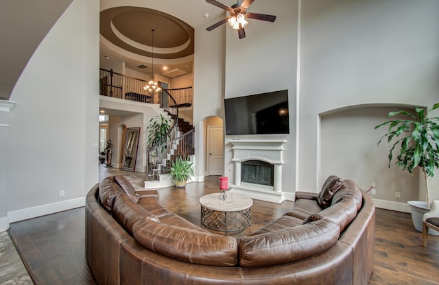 living area featuring wood finished floors, stairway, ceiling fan with notable chandelier, and baseboards