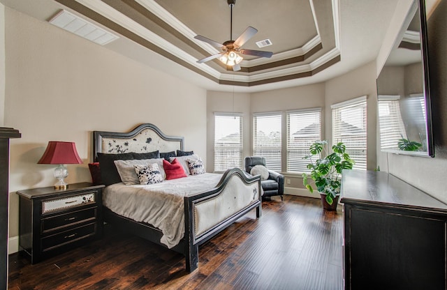 bedroom with dark wood finished floors, visible vents, a tray ceiling, and ornamental molding