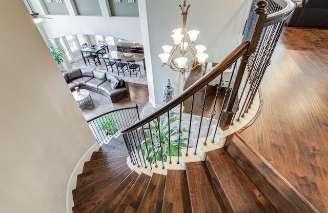staircase featuring ceiling fan with notable chandelier, baseboards, and hardwood / wood-style floors