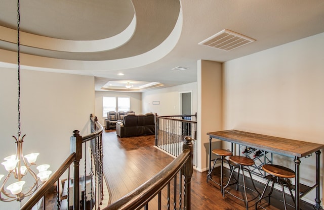 hallway featuring visible vents, a tray ceiling, an upstairs landing, dark wood-style floors, and a notable chandelier