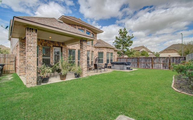 rear view of house with a fenced backyard, a lawn, brick siding, and a patio