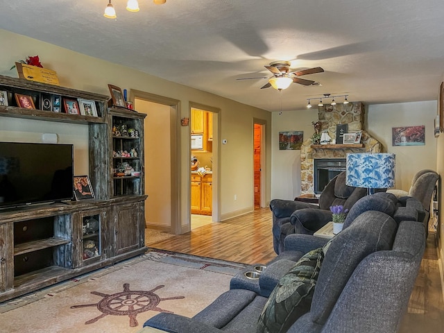 living area with wood finished floors, rail lighting, a stone fireplace, and ceiling fan