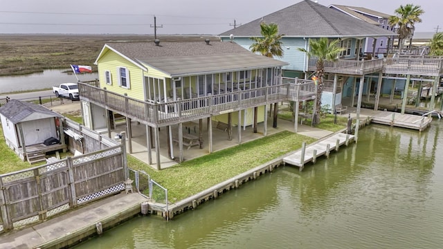 back of property with a deck with water view, a patio area, a sunroom, and fence