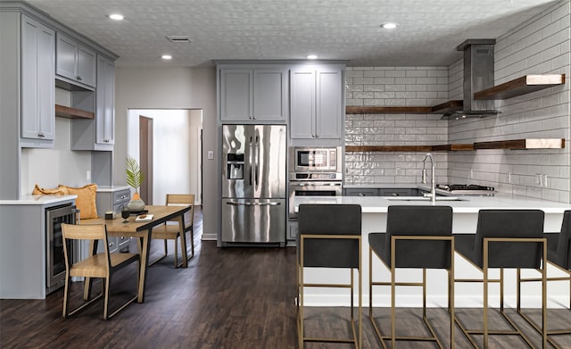 kitchen with gray cabinets, open shelves, appliances with stainless steel finishes, a peninsula, and wall chimney range hood