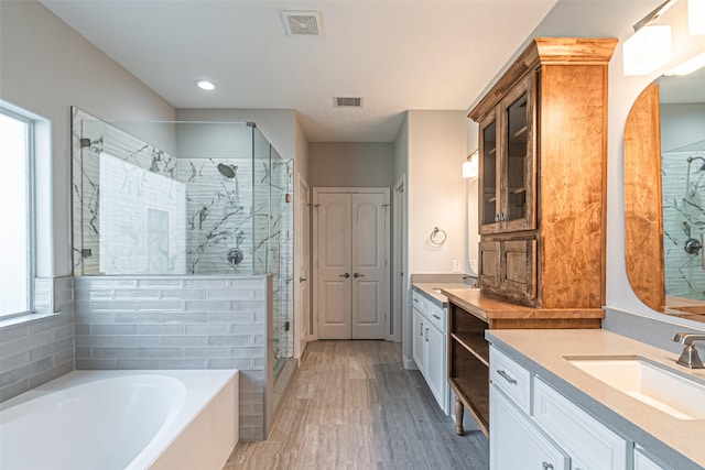 full bathroom with visible vents, a garden tub, two vanities, a stall shower, and a sink