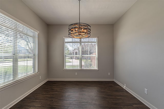 empty room with a chandelier, dark wood finished floors, and baseboards