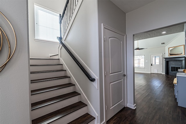 staircase with visible vents, a ceiling fan, wood finished floors, baseboards, and a brick fireplace