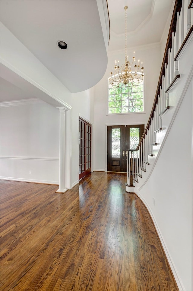 entryway with an inviting chandelier, french doors, crown molding, stairs, and wood finished floors