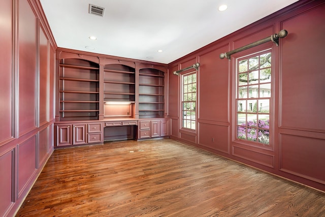 unfurnished office featuring a decorative wall, visible vents, recessed lighting, wood finished floors, and built in study area