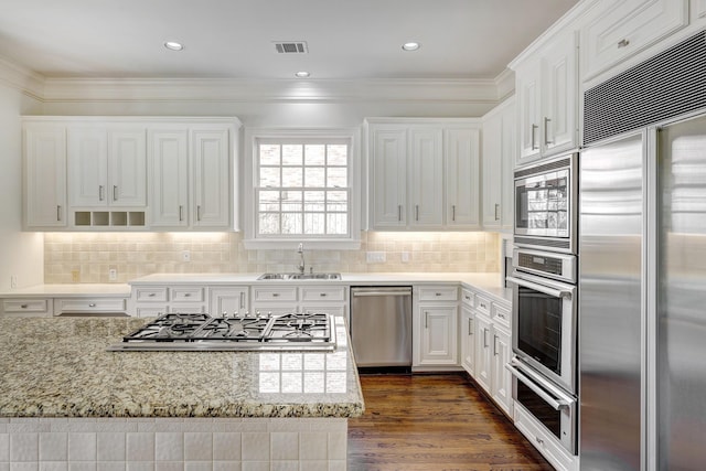 kitchen with white cabinets, built in appliances, a sink, and visible vents