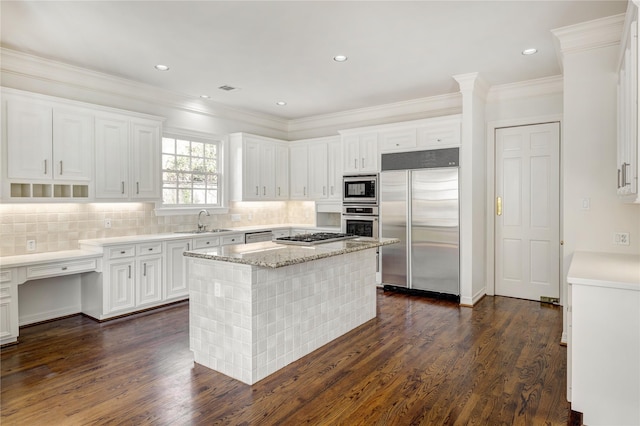 kitchen with dark wood finished floors, white cabinetry, a kitchen island, a sink, and built in appliances