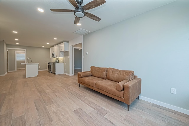 living room with light wood finished floors, visible vents, and baseboards