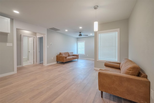 living area featuring visible vents, a ceiling fan, light wood-style flooring, and baseboards