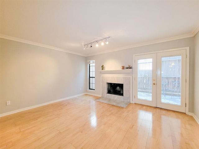 unfurnished living room featuring crown molding, french doors, a fireplace, light wood-style flooring, and baseboards