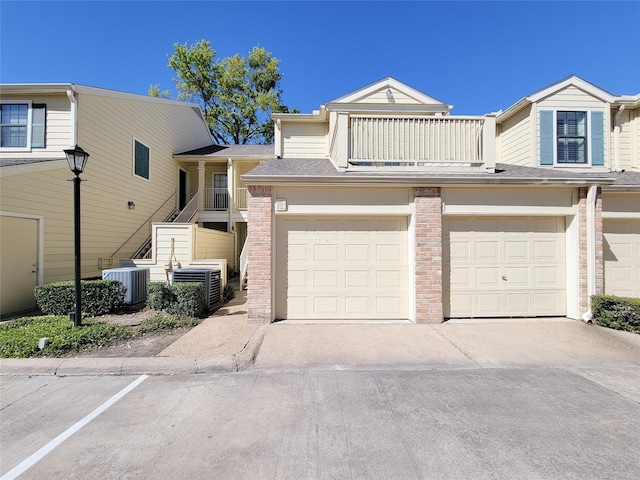 view of property featuring a balcony, an attached garage, central AC unit, and stairway