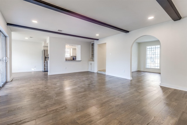 unfurnished living room featuring wood finished floors, arched walkways, baseboards, and beam ceiling