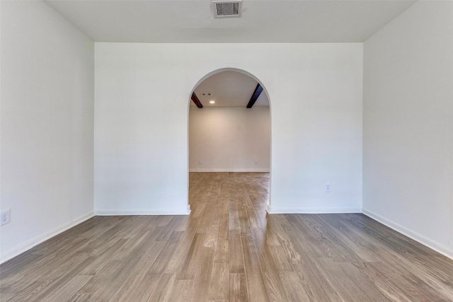 unfurnished room with arched walkways, baseboards, visible vents, and wood finished floors