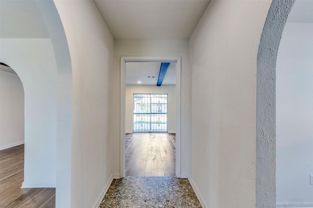 corridor with arched walkways, baseboards, and wood finished floors