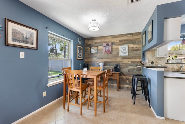 dining room featuring light tile patterned flooring, baseboards, wood walls, and a textured ceiling