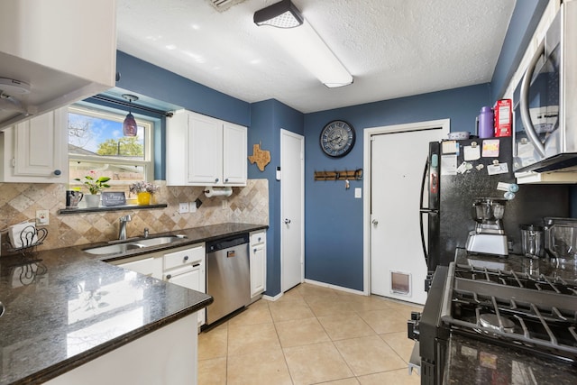 kitchen with a sink, dark countertops, light tile patterned flooring, white cabinets, and black appliances