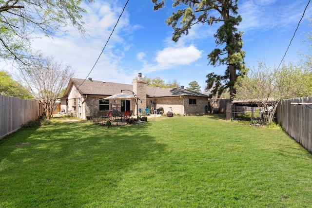 rear view of property with a lawn, a chimney, a fenced backyard, and a patio area