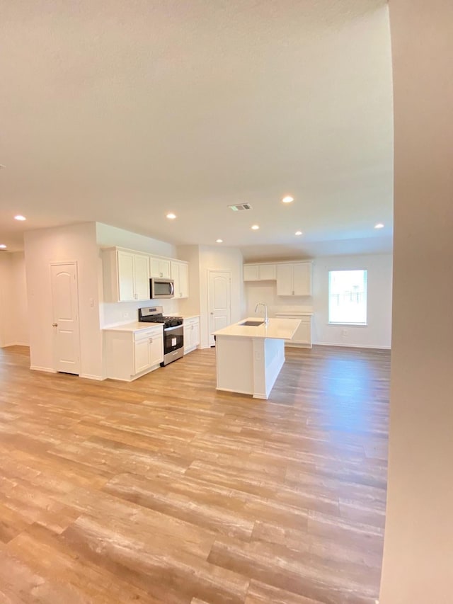 kitchen with light wood-style flooring, appliances with stainless steel finishes, a sink, white cabinetry, and open floor plan