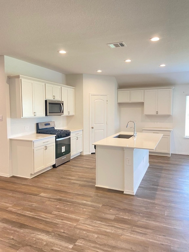 kitchen featuring wood finished floors, appliances with stainless steel finishes, a sink, white cabinetry, and visible vents