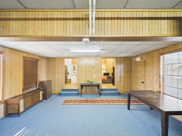 interior space featuring a drop ceiling, carpet floors, and wooden walls