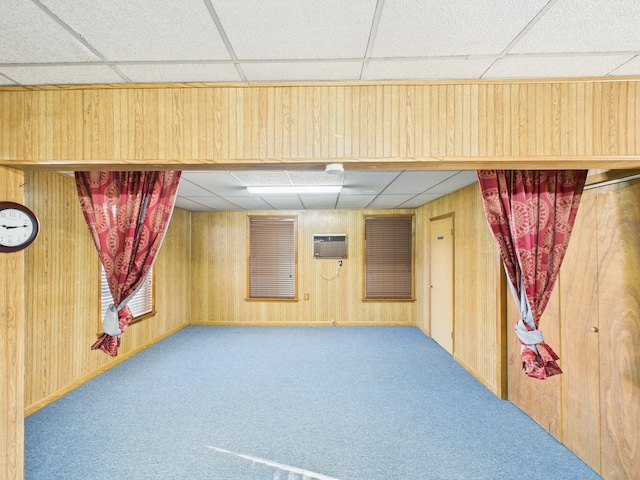 finished basement featuring a drop ceiling, an AC wall unit, and wooden walls