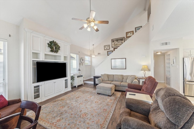living area featuring visible vents, wood finished floors, ceiling fan, stairway, and high vaulted ceiling