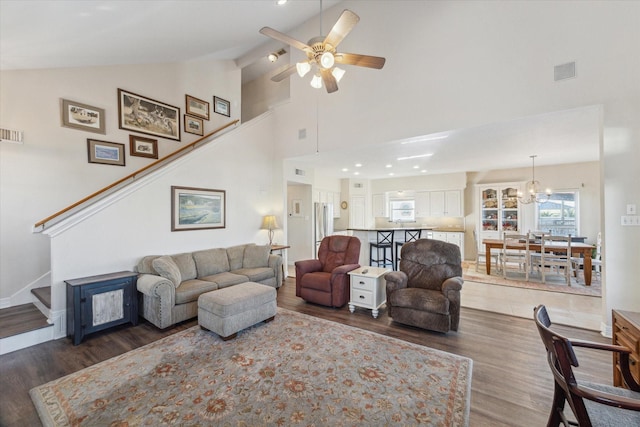 living area with stairs, high vaulted ceiling, wood finished floors, and ceiling fan with notable chandelier