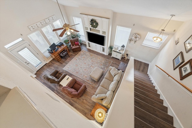 living room featuring ceiling fan, high vaulted ceiling, baseboards, wood finished floors, and stairway