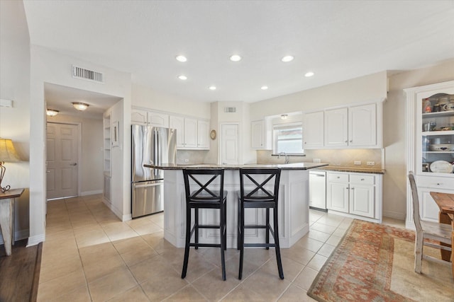 kitchen with white cabinets, dishwasher, a kitchen breakfast bar, freestanding refrigerator, and visible vents