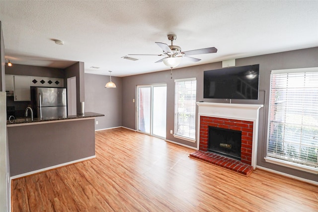 unfurnished living room with ceiling fan, visible vents, a fireplace, a sink, and light wood-style flooring