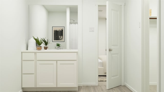 corridor with light wood-style floors, baseboards, and a sink