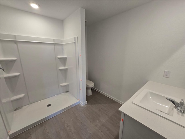 bathroom featuring vanity, toilet, baseboards, wood finished floors, and a stall shower