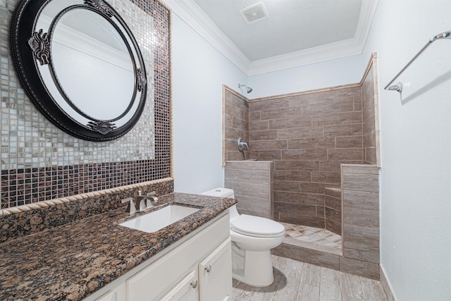 bathroom with vanity, visible vents, tiled shower, crown molding, and toilet