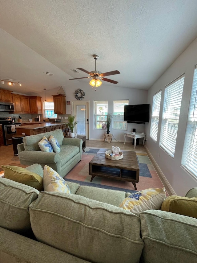 living room with visible vents, a textured ceiling, baseboards, lofted ceiling, and ceiling fan