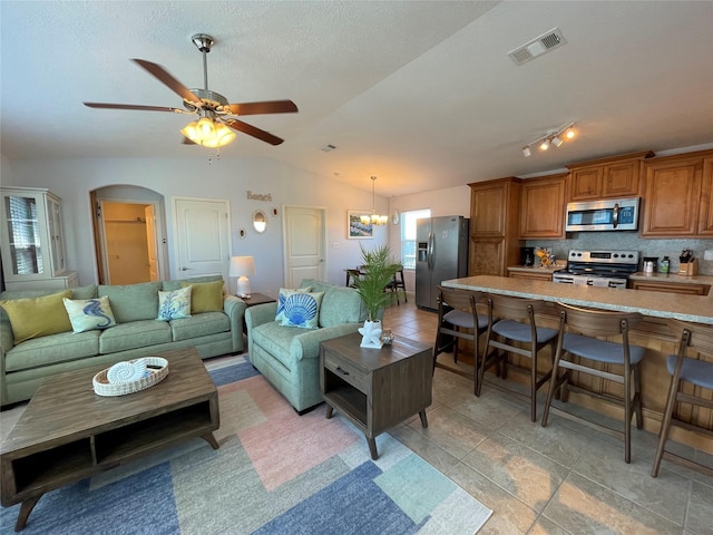 living room featuring visible vents, ceiling fan with notable chandelier, a textured ceiling, arched walkways, and vaulted ceiling