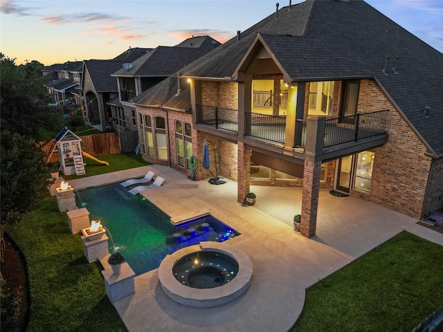 1038 Bolivar Point Ln, Friendswood, TX 77546 - back of house at dusk featuring a balcony, roof with shingles, brick siding, fence, and a patio