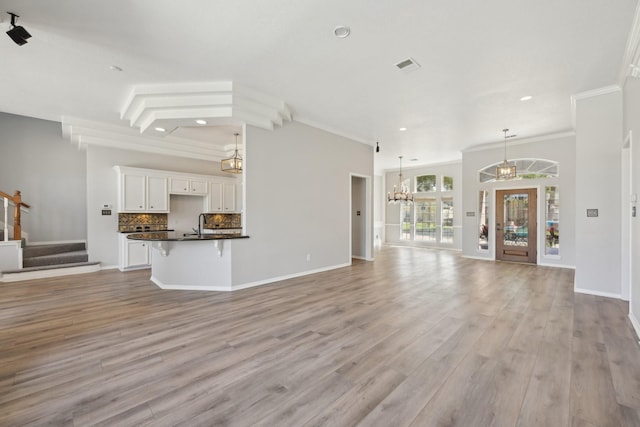 unfurnished living room with crown molding, an inviting chandelier, recessed lighting, light wood finished floors, and stairs