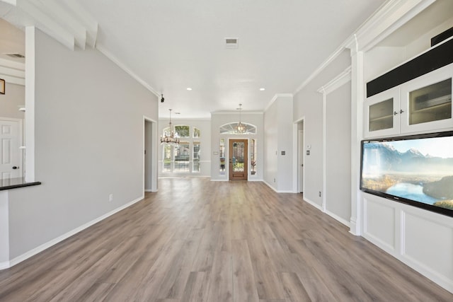 unfurnished living room featuring crown molding, light wood-style flooring, visible vents, baseboards, and an inviting chandelier