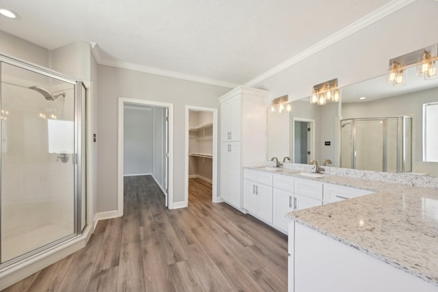 bathroom with crown molding, a stall shower, wood finished floors, vanity, and a walk in closet