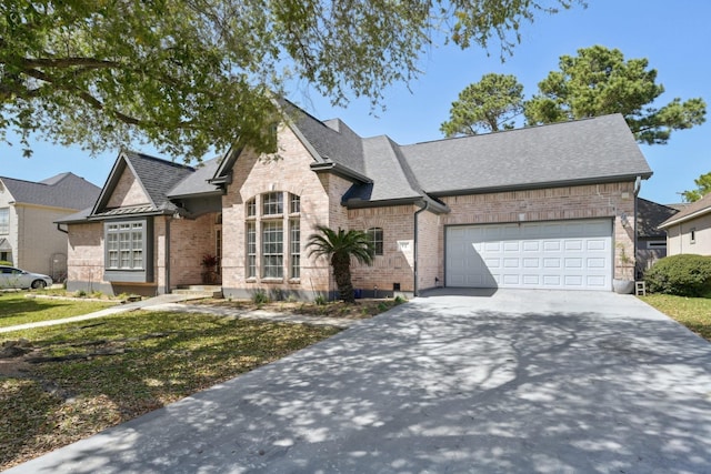 french country home with a garage, brick siding, driveway, and roof with shingles