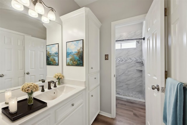 full bath featuring wood finished floors, vanity, baseboards, and tiled shower