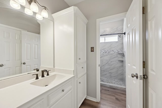 bathroom with a tile shower, baseboards, wood finished floors, and vanity